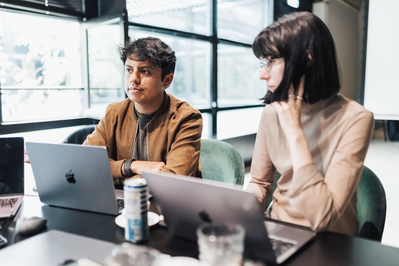 Young professionals collaborate on laptops in a bright, modern office space. Coworking space equipment checklist for new owners