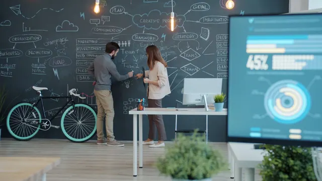 Two people collaborating on a chalkboard with a bicycle Colleagues male and female are talking about business and taking notes on chalkboard wall standing together discussing work. Coworking space KPIs owners should track monthly