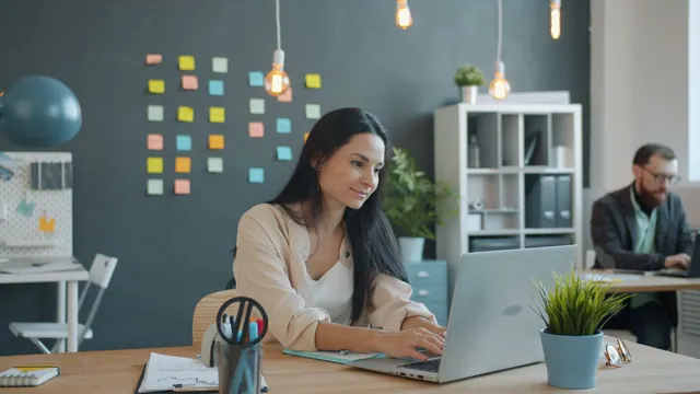 Two young adults working at laptops in a modern, creative office space. New vs used coworking space equipment: cost guide